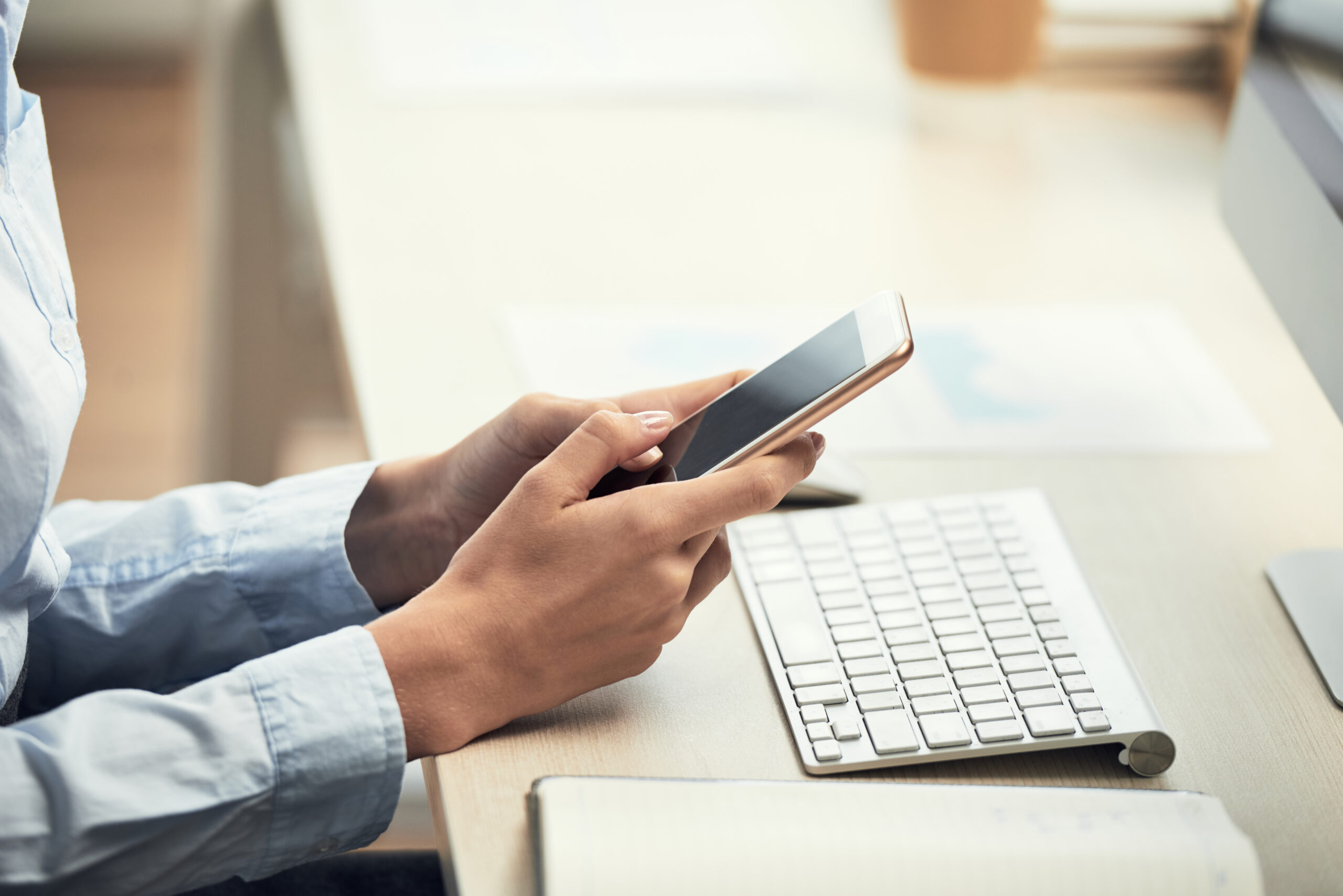 Crop side view of woman using smartphone while sitting at computer desk in daylight