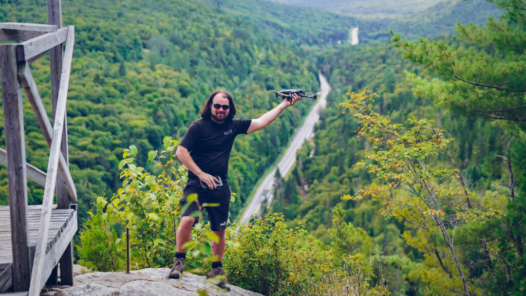 Dominic devant un pont dans une forêt.
